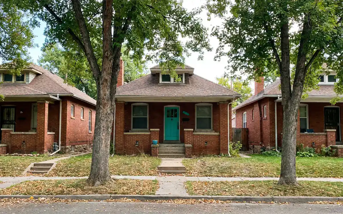 Row of older brick bungalows, one with a teal front door, on a tree-lined street